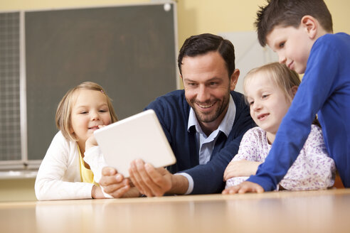 Lehrerin mit Schülern, die ein digitales Tablet im Klassenzimmer benutzen - MFRF000099