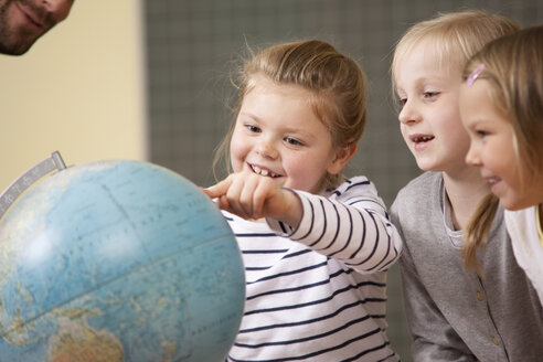 Lächelnde Schulmädchen, die auf einen Globus im Klassenzimmer zeigen - MFRF000132