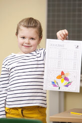 Porträt einer lächelnden Schülerin im Klassenzimmer, die ein Arbeitsblatt hält - MFRF000135