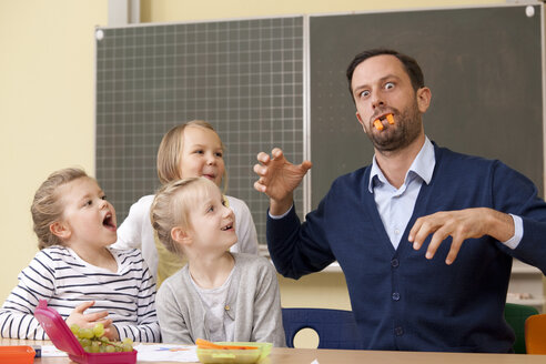 Schulmädchen, die einen verspielten Lehrer mit Karottenstäbchen ansehen - MFRF000139