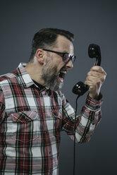 Man screaming into retro telephone in front of grey background - IPF000208