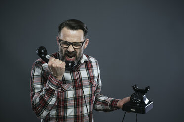 Man screaming into retro telephone in front of grey background - IPF000209