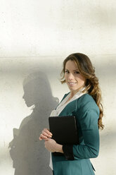 Smiling businesswoman at concrete wall holding digital tablet - BFRF001003