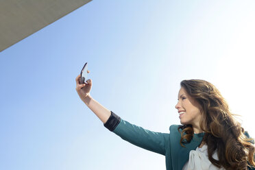 Lächelnde Geschäftsfrau nimmt Selfie unter blauem Himmel - BFRF000987