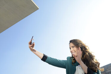 Smiling businesswoman taking selfie under blue sky - BFRF000988