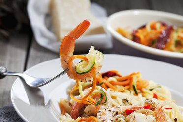Spaghetti mit Scampis und Gemüse auf Teller, Karotten- und Zucchinispiralen, Gabel, Nahaufnahme - CSF024744