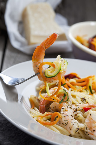 Spaghetti mit Scampis und Gemüse auf Teller, Karotten- und Zucchinispiralen, Gabel, Nahaufnahme, lizenzfreies Stockfoto