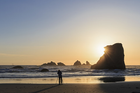 USA, Oregon, Bandon, Bandon Beach, Felsnadeln bei Sonnenuntergang, Fotografin am Strand, lizenzfreies Stockfoto