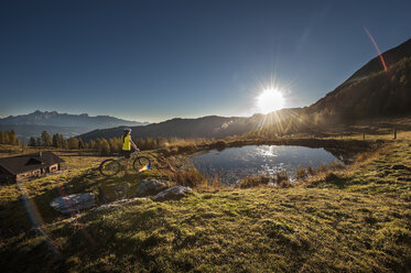 Österreich, Altenmarkt-Zauchensee, junge Frau mit Mountainbike in den Bergen bei Sonnenaufgang - HHF005188