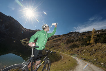 Austria, Altenmarkt-Zauchensee, young man with mountain bike refrshing at mountain lake - HHF005201