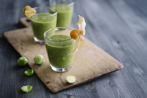 Grüner Smoothie mit Rosenkohl, Banane und Apfelsaft garniert mit Physalis, lizenzfreies Stockfoto