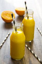Orangen-Smoothie in Glasflaschen, Strohhalme auf Holz - SARF001455