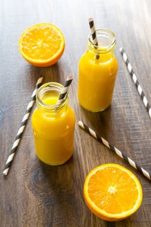 Orangen-Smoothie in Glasflaschen, Strohhalme auf Holz - SARF001456