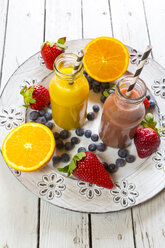 Orangen- und Erdbeer-Smoothie in Glasflaschen und Früchte auf Teller - SARF001459