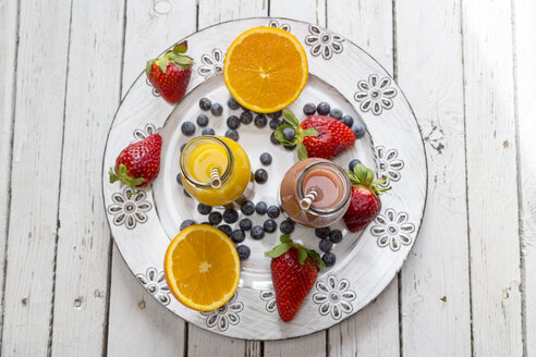 Orangen- und Erdbeer-Smoothie in Glasflaschen und Früchte auf Teller - SARF001460