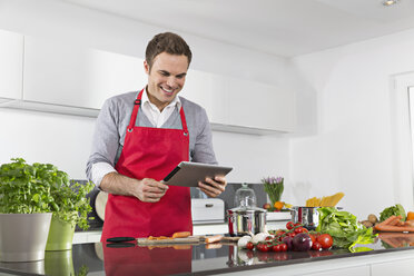 Lächelnder Mann, der beim Kochen ein digitales Tablet benutzt - PDF000831