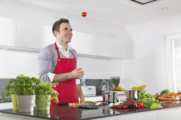 Smiling man juggling with tomatoes in kitchen - PDF000833