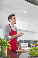 Smiling man juggling with garlic bulb in kitchen - PDF000834