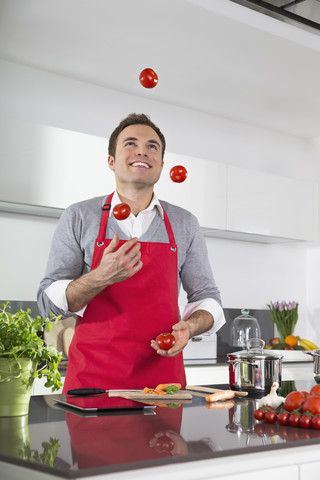 Lächelnder Mann, der in der Küche mit Tomaten jongliert, lizenzfreies Stockfoto