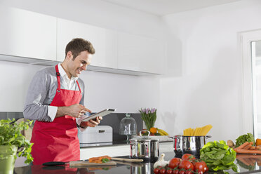 Smiling man looking at digital tablet in the kitchen - PDF000839