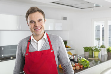 Porträt eines lächelnden Mannes mit roter Schürze in der Küche - PDF000841