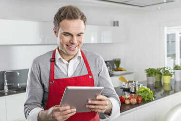 Lächelnder Mann mit Blick auf ein digitales Tablet in der Küche - PDF000844