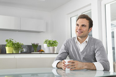 Lächelnder Mann sitzt in der Küche mit einer Tasse Kaffee - PDF000848