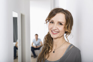 Porträt einer lächelnden Frau im Korridor, während ein Mann im Hintergrund wartet - PDF000870