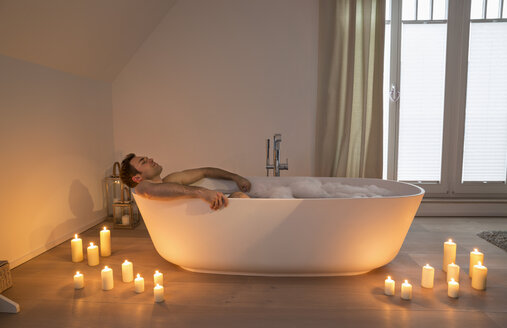 Man relaxing in bathtub with lighted candles arround - PDF000876