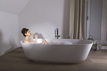 Woman relaxing in modern bathtub drinking champagne - PDF000885