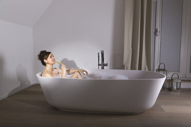 Lächelnde Frau entspannt sich in einer modernen Badewanne mit einem Glas Champagner - PDF000886