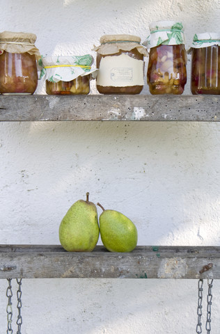 Row of preserving jars of pear chutneys and two fresh pears on wooden ladder stock photo