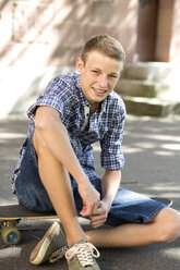 Smiling teenage boy sitting on skateboard - DRF001480