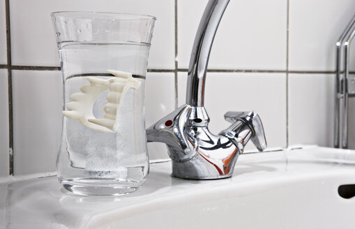 Vampire dentures in water glass on bathroom sink - STK001204
