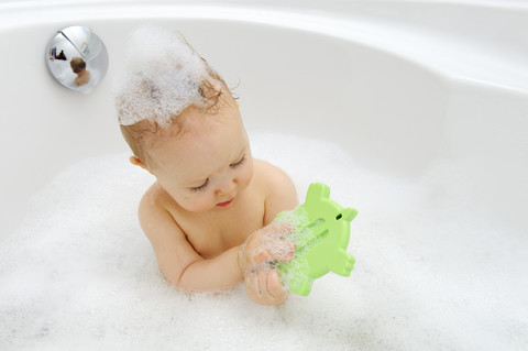 Babymädchen mit Thermometer in einer Badewanne, lizenzfreies Stockfoto