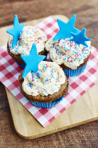 Cupcakes mit weißem Zuckerguss, bunten Streuseln und einem blauen Stern aus Fondant, lizenzfreies Stockfoto