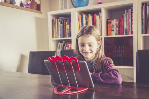Kleines Mädchen mit digitalem Tablet vor einem Bücherregal, lizenzfreies Stockfoto
