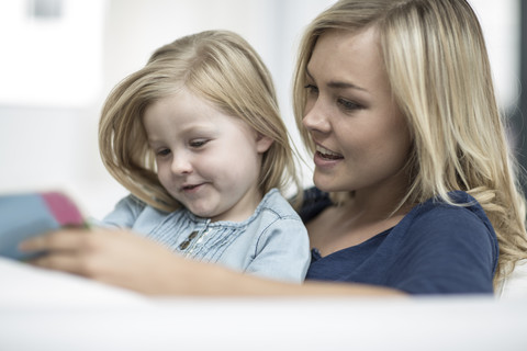 Mutter und kleine Tochter sitzen auf einer Couch und lesen ein Buch, lizenzfreies Stockfoto