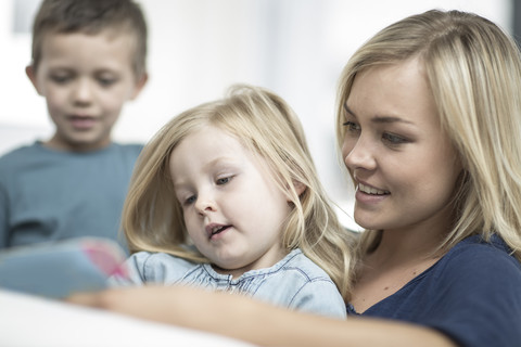 Mutter und kleine Tochter sitzen auf einer Couch und lesen ein Buch, lizenzfreies Stockfoto