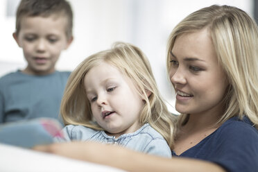 Mother and little daughter sitting on a couch reading a book - ZEF004009