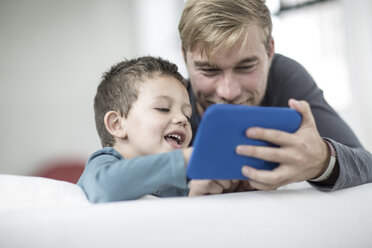 Vater und kleiner Sohn auf der Couch mit Blick auf ein Tablet - ZEF004010