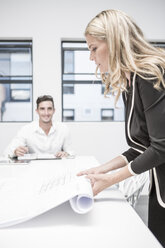 Businesswoman in office rolling up constuction plan - ZEF004525