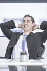 Lächelnder Geschäftsmann im Büro sitzend, Hände hinter dem Kopf - ZEF004578