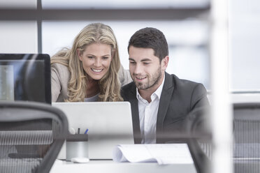 Smiling businessman and businesswoman in office looking at laptop - ZEF004659