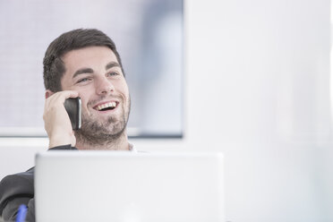 Lächelnder Geschäftsmann im Büro mit Laptop und Mobiltelefon - ZEF004666