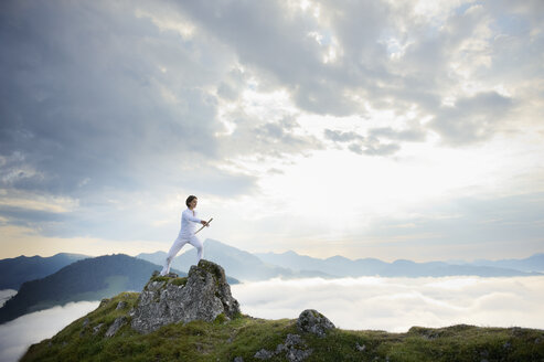 Austria, Kranzhorn, Mid adult woman exercising stick fighting on mountain top - MAOF000056