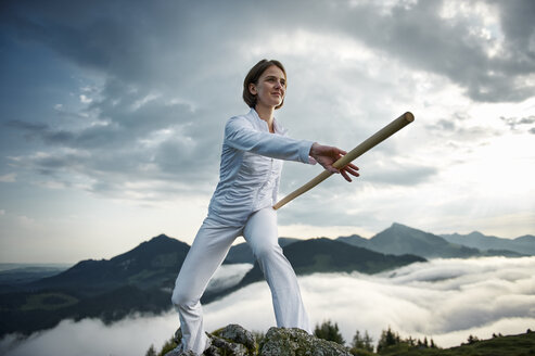 Austria, Kranzhorn, Mid adult woman exercising stick fighting on mountain top - MAOF000002