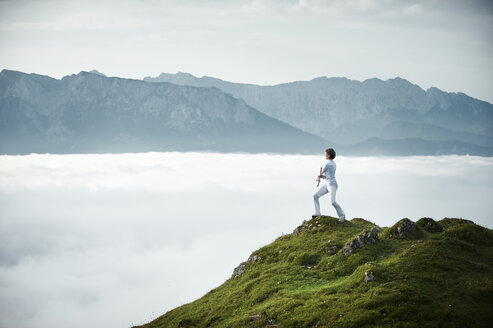 Austria, Kranzhorn, Mid adult woman exercising stick fighting on mountain top - MAOF000003