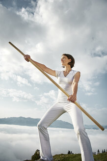 Austria, Kranzhorn, Mid adult woman exercising stick fighting on mountain top - MAOF000004