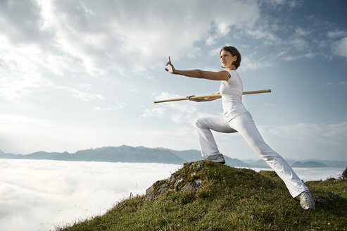 Austria, Kranzhorn, Mid adult woman exercising stick fighting on mountain top - MAOF000057